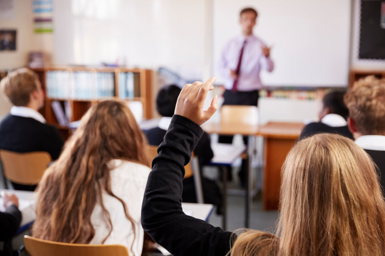 High school children in a classroom, learning from a teacher